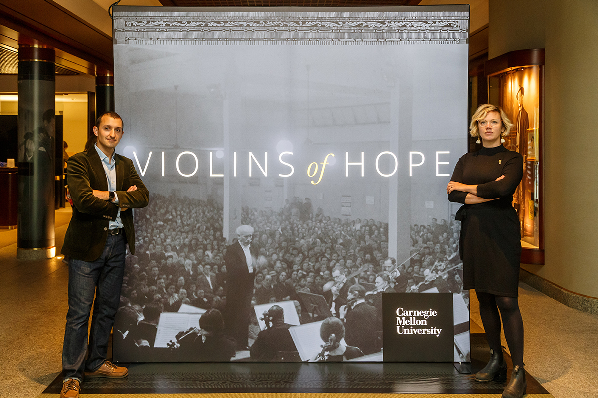 CMU Libraries’ Creative Director, Heidi Wiren Kebe and Curator of Special Collections, Sam Lemley stand at the entrance to the Violins of Hope exhibition.