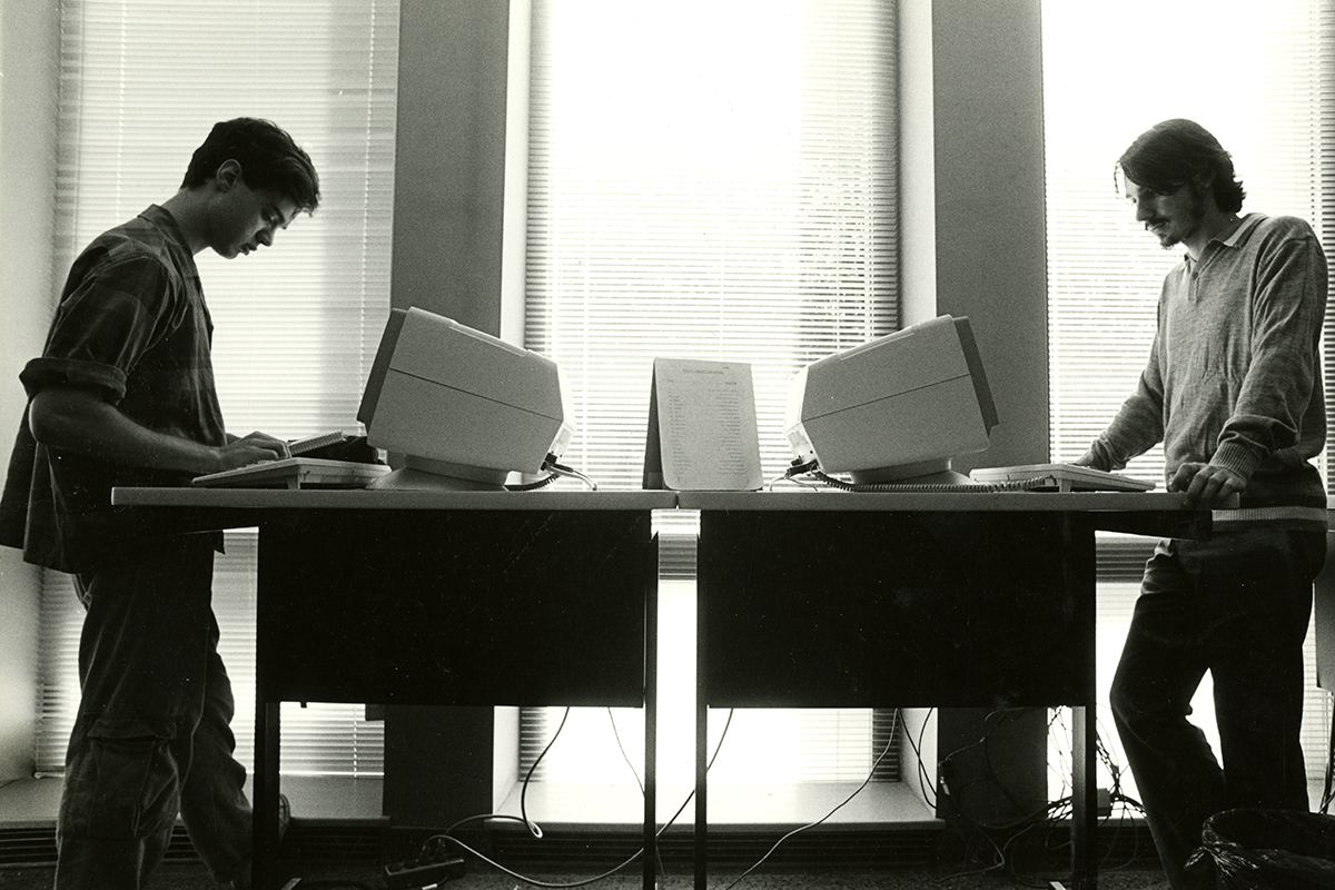 Two students work on old computers in a black and white photo