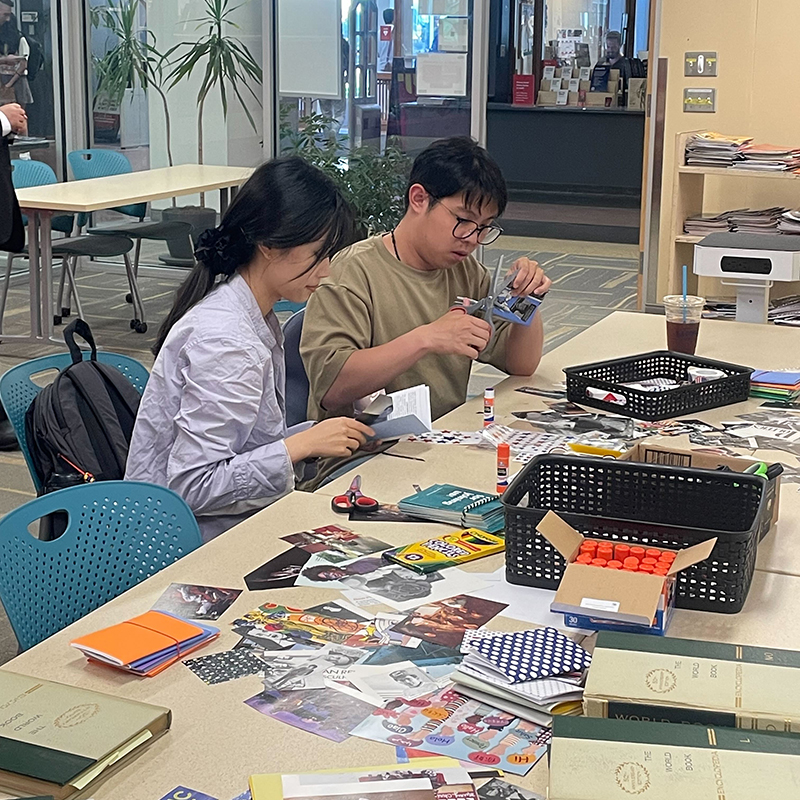 Two students use pages from discarded magazines and other craft materials to decorate the covers of their Constitutions.
