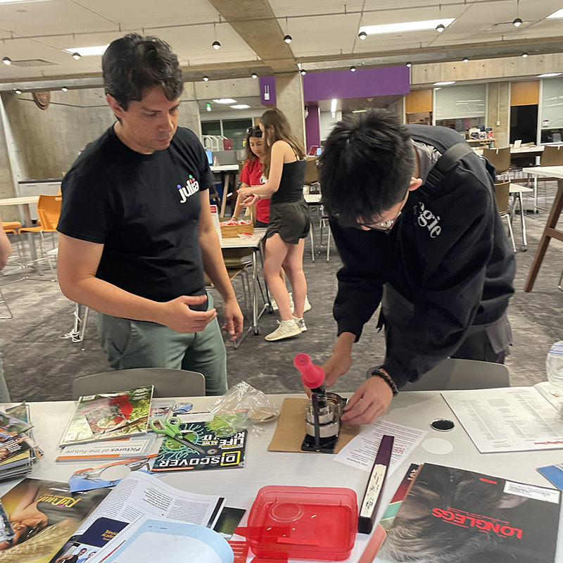 In Sorrells Library, Research Data Services Librarian Alfredo González-Espinoza helps a student make buttons featuring graphics from discarded library materials.