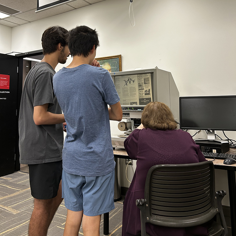 Stacks Manager Gloria Henning introduces two students to a microfilm reader as part of the Obsolete Technology Petting Zoo. Microfilm was a convenient way to store large amounts of text prior to the invention of modern computers.